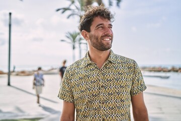 Young hispanic man smiling confident walking at seaside