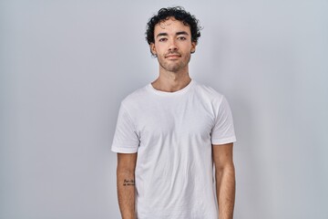 Hispanic man standing over isolated background relaxed with serious expression on face. simple and...