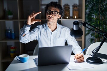 Hispanic man working at the office at night smiling and confident gesturing with hand doing small...