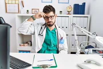 Young man with beard wearing doctor uniform and stethoscope at the clinic worried and stressed about a problem with hand on forehead, nervous and anxious for crisis