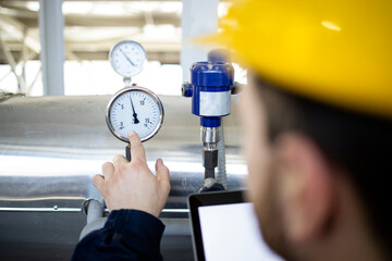 Heating plant worker reading water pipe pressure in energy factory.