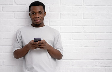 Black young man using smartphone over white brick background, finger, reading social media internet, typing text or shopping online, copyspace 