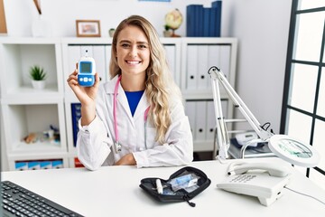Young beautiful doctor woman holding glucose meter looking positive and happy standing and smiling...