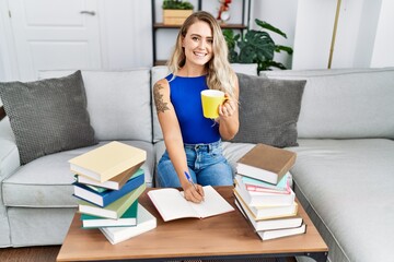 Young woman sitting on sofa studying and drinking coffee at home