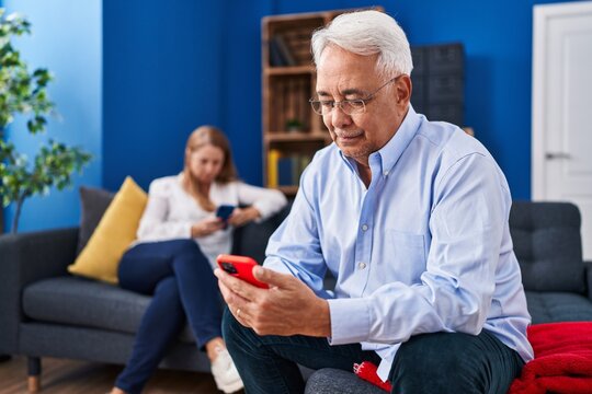 Middle age man and woman couple using smartphone sitting on sofa at home