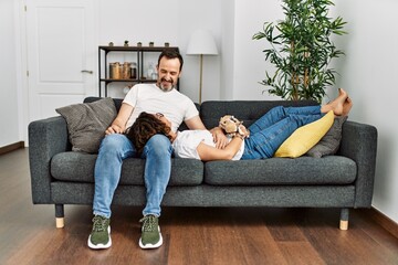 Middle age hispanic couple relaxed sitting on the sofa with dog at home.