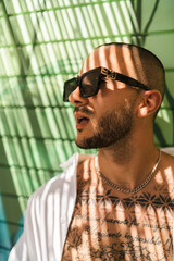 Obraz premium Chico joven guapo musculoso en zona de sombra con gafas de sol sonriendo, posando y tomándose selfies