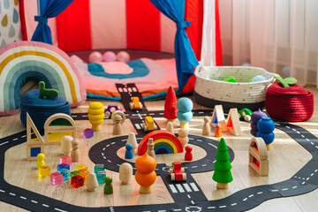 Children's room with a play tent and toys. A toy town built in a children's room. Car track, toy cars, trees and wooden blocks for games in playroom. Educational game for toddler in modern nursery.