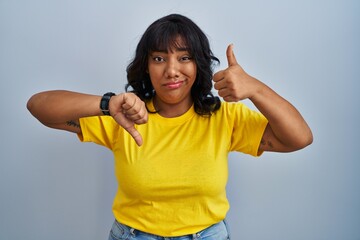 Hispanic woman standing over blue background doing thumbs up and down, disagreement and agreement expression. crazy conflict