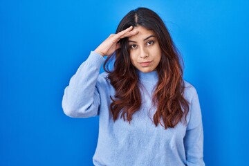 Naklejka premium Hispanic young woman standing over blue background worried and stressed about a problem with hand on forehead, nervous and anxious for crisis