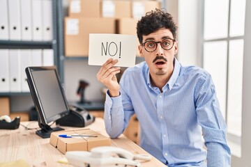 Hispanic man working at small business ecommerce holding no banner scared and amazed with open mouth for surprise, disbelief face