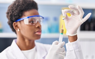 African american woman wearing scientist uniform holding vaccine at laboratory