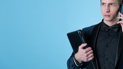 A successful and positive young man in a business suit with a laptop in his hands, talking on the phone, photo on blue