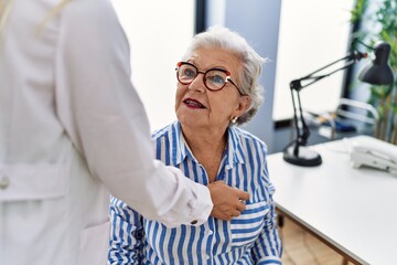 Senior grey-haired woman patient having medical consultation auscultating heart at clinic