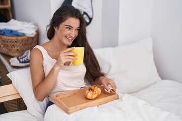 Young hispanic woman having breakfast sitting on bed at bedroom