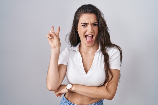 Young teenager girl standing over white background smiling with happy face winking at the camera doing victory sign with fingers. number two.