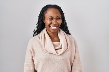 Fototapeta premium African woman standing over white background winking looking at the camera with sexy expression, cheerful and happy face.