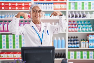 Middle age woman with tattoos working at pharmacy drugstore looking confident with smile on face, pointing oneself with fingers proud and happy.