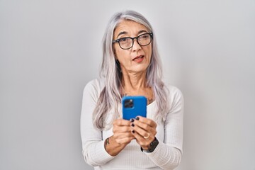 Middle age woman with grey hair using smartphone typing message winking looking at the camera with sexy expression, cheerful and happy face.