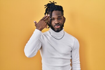 African man with dreadlocks wearing turtleneck sweater over yellow background shooting and killing oneself pointing hand and fingers to head like gun, suicide gesture.