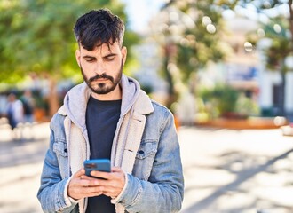 Fototapeta premium Young hispanic man using smartphone at park