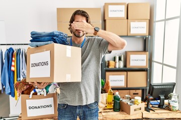 Handsome middle age man holding donations box for charity at volunteer stand covering eyes with hand, looking serious and sad. sightless, hiding and rejection concept