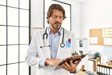 Middle age caucasian man wearing doctor uniform reading diagnosis al clinic