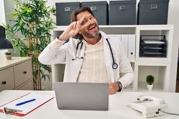 Handsome middle age doctor man working at the clinic doing peace symbol with fingers over face, smiling cheerful showing victory