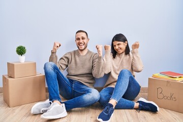 Young couple moving to a new home celebrating surprised and amazed for success with arms raised and...
