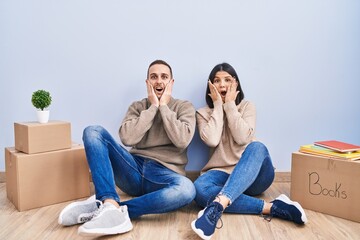 Young couple moving to a new home afraid and shocked, surprise and amazed expression with hands on face