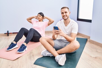 Fototapeta na wymiar Man and woman couple smiling confident training abs exercise using smartphone at sport center