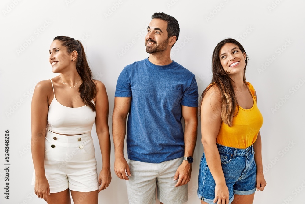 Wall mural Group of young hispanic people standing over isolated background looking away to side with smile on face, natural expression. laughing confident.