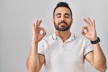 Young hispanic man with beard wearing casual clothes over white background relaxed and smiling with eyes closed doing meditation gesture with fingers. yoga concept.