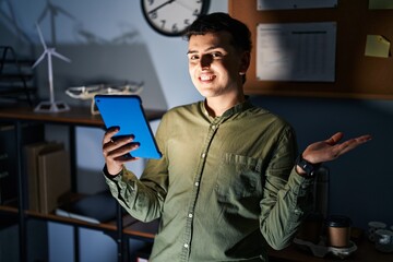 Non binary person using touchpad device at night pointing aside with hands open palms showing copy...