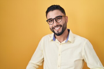 Fototapeta premium Hispanic young man wearing business clothes and glasses smiling cheerful with open arms as friendly welcome, positive and confident greetings