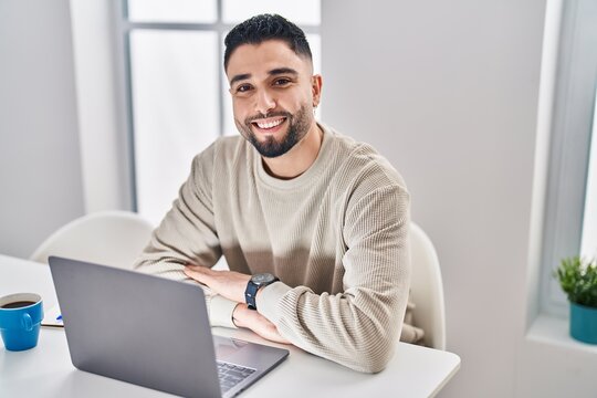 Young arab man using laptop and drinking coffee sitting on table at home