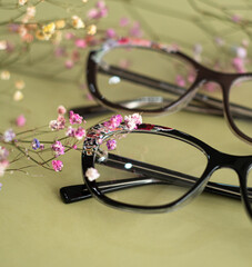 glasses for vision lie on the background of a green table and flowers nearby