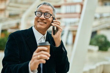 Middle age southeast asian man speaking on the phone and drinking a cup of coffee at the city