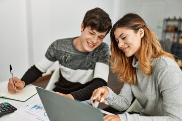 Young couple smiling happy working using laptop sitting on the table at home.