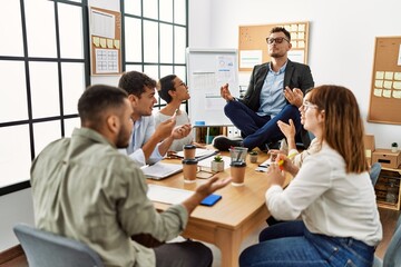 Businessman enjoys meditating during meeting. Sitting on desk near arguing partners at the office.