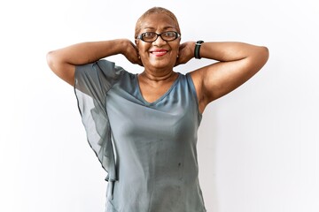 Fototapeta premium Mature hispanic woman wearing glasses standing over isolated background relaxing and stretching, arms and hands behind head and neck smiling happy
