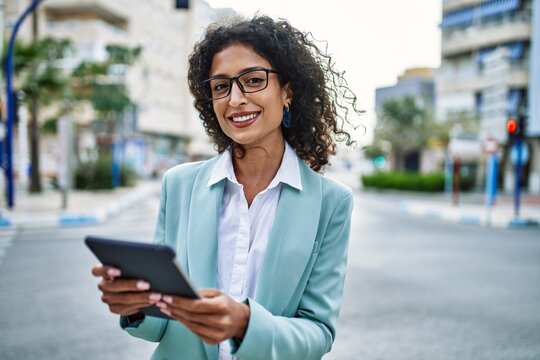 Young hispanic business woman wearing professional look smiling confident at the city using touchpad device