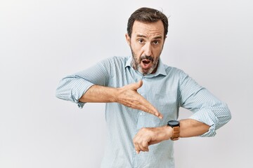 Middle age hispanic man with beard standing over isolated background in hurry pointing to watch...