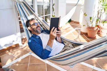 Middle age man reading book lying on hammock at terrace home