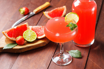 Fresh grapefruit juice in a glass with grapefruit pieces, lime and mint on a wooden background.