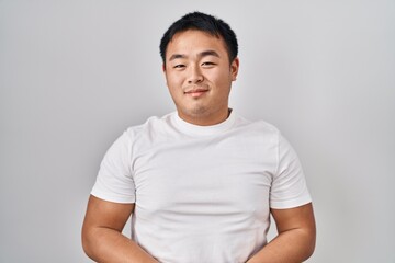 Young chinese man standing over white background with hands together and crossed fingers smiling relaxed and cheerful. success and optimistic