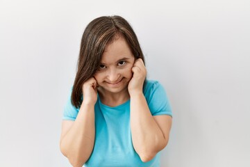 Young down syndrome woman standing over isolated background covering ears with fingers with annoyed expression for the noise of loud music. deaf concept.