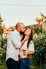 Portrait of a smiling  happy couple kissing    in a Vineyard toasting wine. Beautiful  brunette woman and bearded muscular man spending time together during grape harvest.