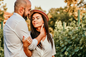 Portrait of a smiling  happy couple kissing    in a Vineyard toasting wine. Beautiful  brunette woman and bearded muscular man spending time together during grape harvest.