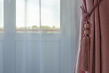 A modern background with a window covered with tulle and a curtain with tassel. Copy space.